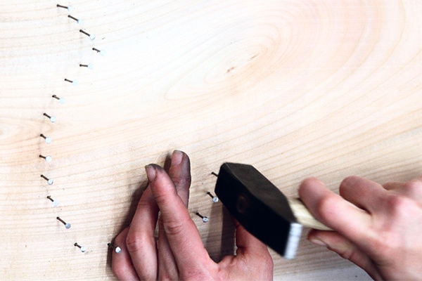 Nägel mit einem Hamme in den Unterrund aus Holz schlagen, sie sind die Vorlage für das sommerliche Fadenbild