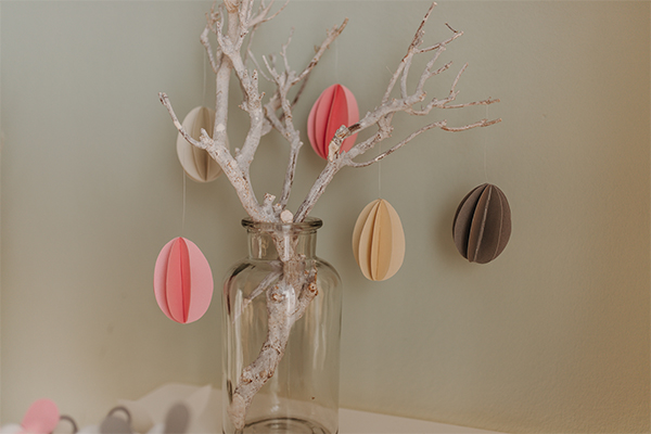 Ostereier aus buntem Papier hängen an einem Zweig, der in einer Vase steckt