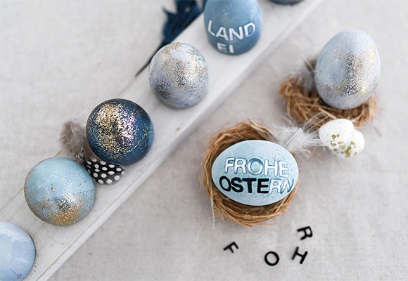 Natürlich gefärbte, bunte Ostereier in blau, verziert mit Schrift und Glitzer