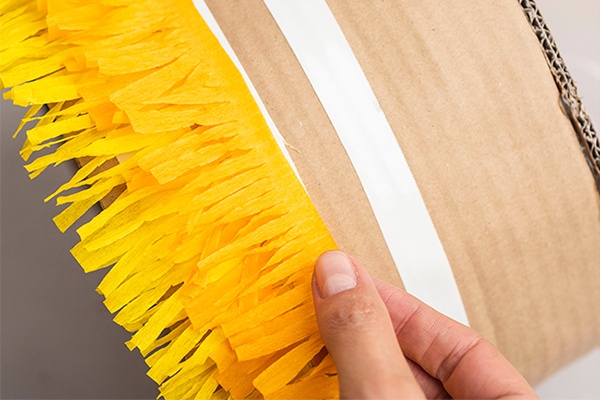 Den Torten-Körper mit den vorbereiteten Fransenbändern nach und nach bekleben, sodass die bunten Fransen sich überlappen