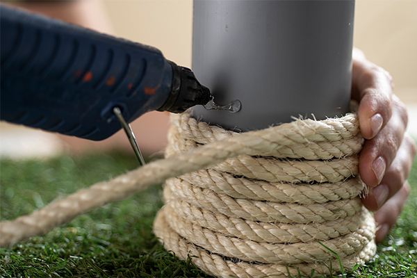 Seil wird mit einer Heißklebepistole an ein Rohr geklebt