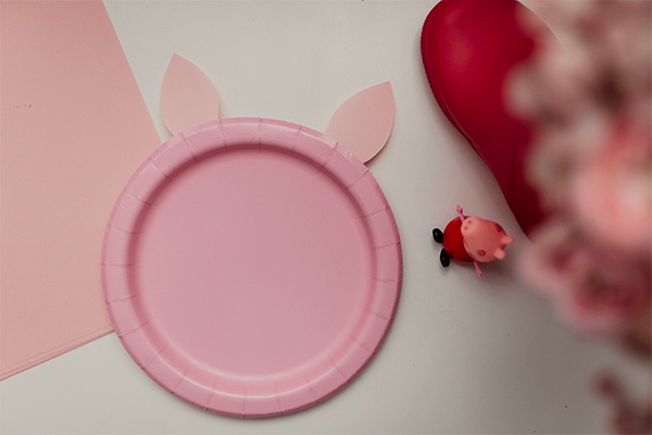 Den Pappteller in pink mit Schweineohren aus Papier verzieren