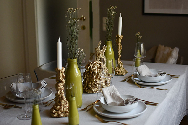 Gedeckter Tisch mit grünen Vasen und goldenen Kerzenständern