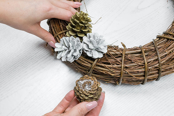 Weiße und goldene Zapfen werden auf einem Kranz befestigt