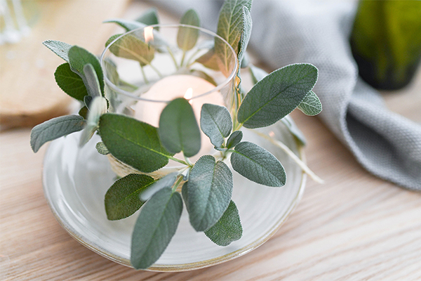 Weinflaschenglas mit einer Kerze und einem Salbeikranz.