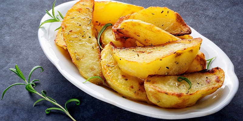 Einige Kartoffelecken auf einem ovalen Teller garniert mit Rosmarin.