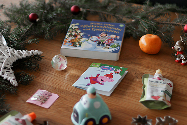 Auf dem Bild ist Kinderspielzeug mit weihnachtlicher Umgebung. Es ist eine Mandarine, ein weihnachtliches Buch, ein Spielzeugauto und vieles mehr auf einem Tisch mit Tannenzweigen.