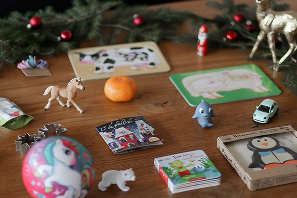 Auf dem Bild ist Kinderspielzeug mit weihnachtlicher Umgebung. Es ist eine Mandarine, ein weihnachtliches Buch, ein Spielzeugauto und vieles mehr auf einem Tisch mit Tannenzweigen.