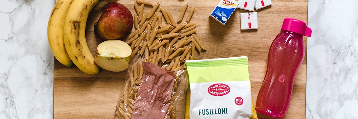 Sportliche Ernährung mit Bananen, Äpfeln, Vollkorn-Nudeln und Traubenzucker 