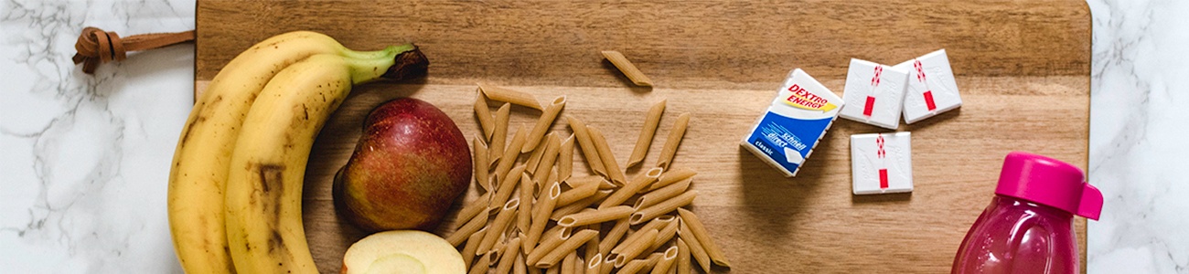 Sportliche Ernährung mit Bananen, Äpfeln, Vollkorn-Nudeln und Traubenzucker 