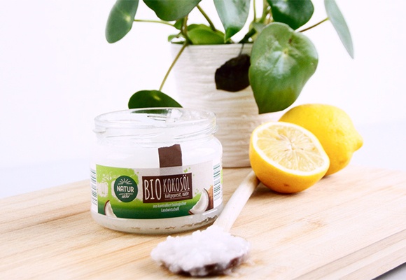 Glas mit Kokosöl auf einem Brett mit Zitronen und einer Pflanze   