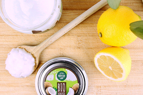 Kokosöl auf einem Holzlöffel neben einer aufgeschnittenen Zitrone