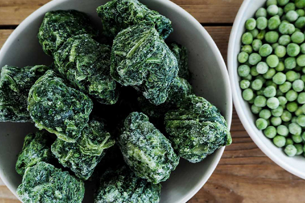 Tiefkühlspinat und Tiefkühlerbsen in einer weißen Schale