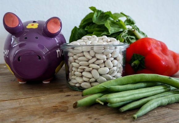 Sparschwein neben einem Glas weißer Bohnen 