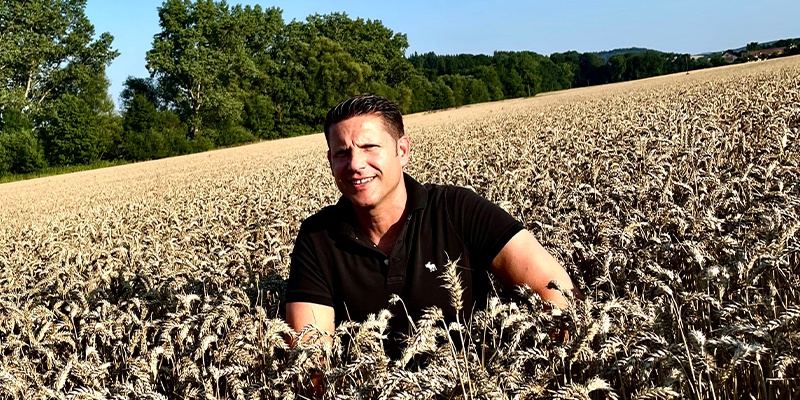 Ein Mann hockt im Getreidefeld.