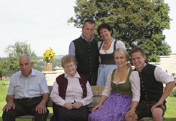 Drei Generationen der Familie Stadlmayr sitzen im Garten auf einer Bank und tragen eine Tracht.