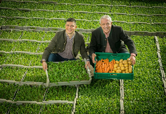 Zwei Männer auf einem Feld präsentieren zwei Gemüsekisten