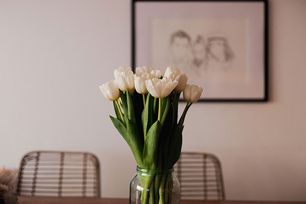 Weiße Tulpen auf einem Esstisch. Im Hintergrund ein gezeichnetes Bild.