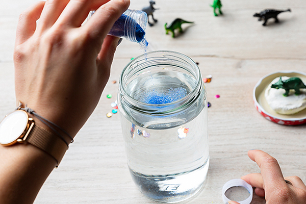 Blauer Glitzer wird in ein Schraubglas mit Wasser gefüllt.