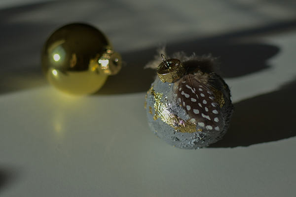 Goldene Christbaumkugel und eine mit Federn in grau