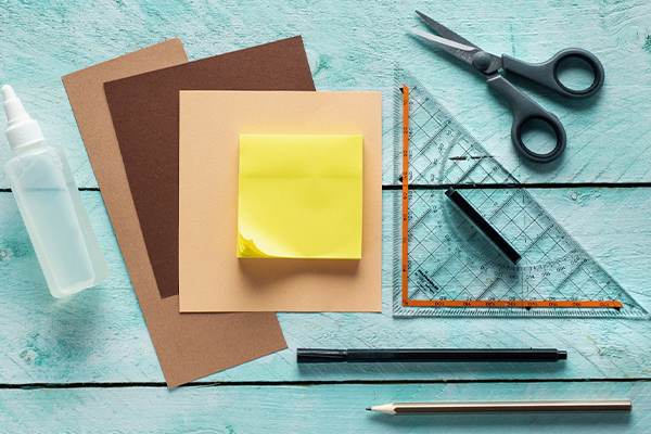 Auf dem Bild sind die Utensilien für die tierischen Notizblöcke ersichtlich. Darunter eine Schere, Stifte, Geodreieck und braunes Papier.
