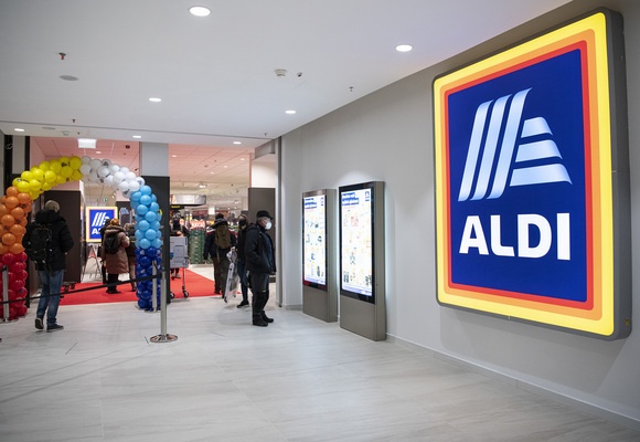 Az ALDI két munkatársa újhagymás ládákat tesz a zöldséges polcokra.