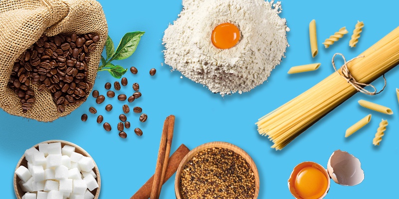 Verschiedene Kochzutaten auf blauem Hintergrund: Kaffee, Zucker, Mehl, Ei, Zimt, Pasta und grüne Blätter.