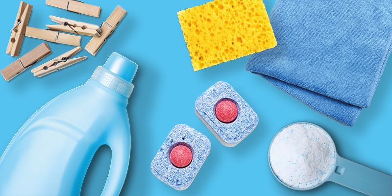 Verschiedene Reinigungs- und Waschmittel auf blauem Hintergrund: Flasche, Waschpods, Schwamm, Tuch, Messlöffel, Wäscheklammern.