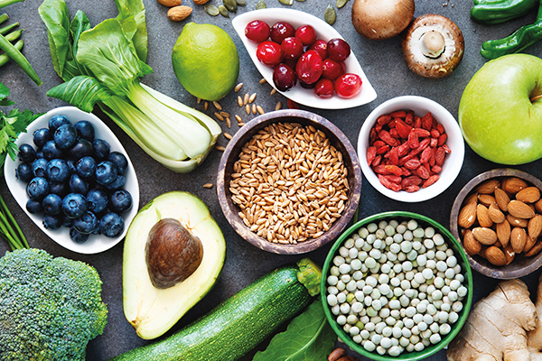 Obst und Gemüse auf einem grauen Hintergrund. Abgebildet sind Heidelbeeren, Avocado, Zucchini, Brokkoli, verschiedene Hülsenfrüchte und Mandeln.