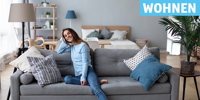 Wohnen: Eine junge Frau sitzt auf einem grauen Sofa.