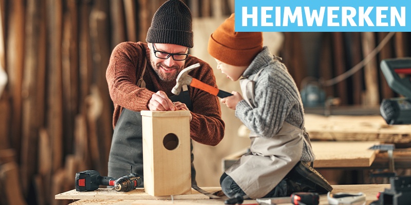 Heimwerken: Ein Kind hämmert ein Vogelhaus, der Vater mit Bart hilft dabei.