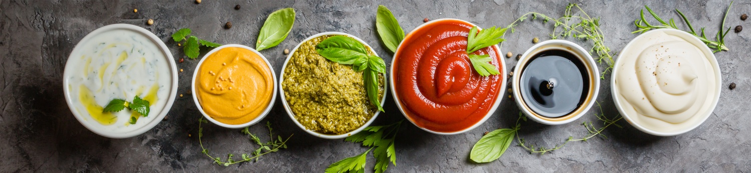 Sechs Keramikschalen mit unterschiedlichen Dips und Soßen.
