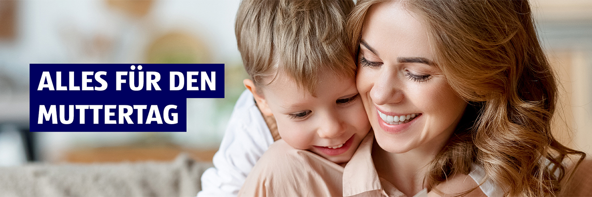 Alles für den Muttertag. Eine Mutter wird von hinten von ihrem Sohn umarmt während sie auf dem Sofa sitzt