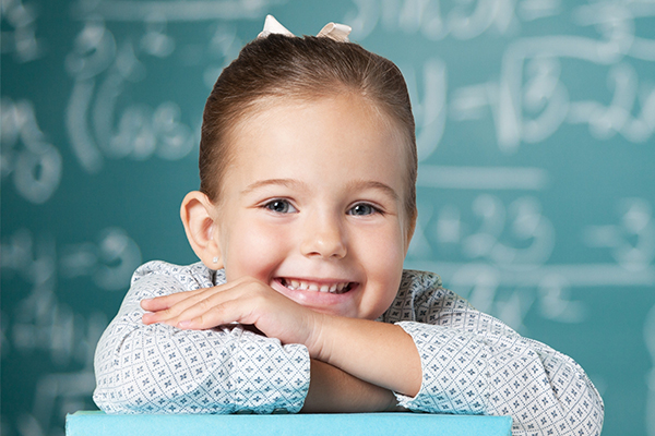 Mädchen lehnt vor der Tafel auf einem Tisch und lächelt.