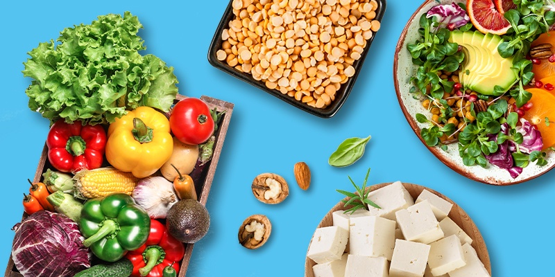 Eine Auswahl frischer, nährstoffreicher Lebensmittel auf blauem Hintergrund, darunter Gemüse, Nüsse und Tofu.