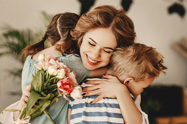 Eine Mutter wird von ihrem kleinen Sohn und ihrer kleinen Tochter umarmt und hat Tulpen in der Hand