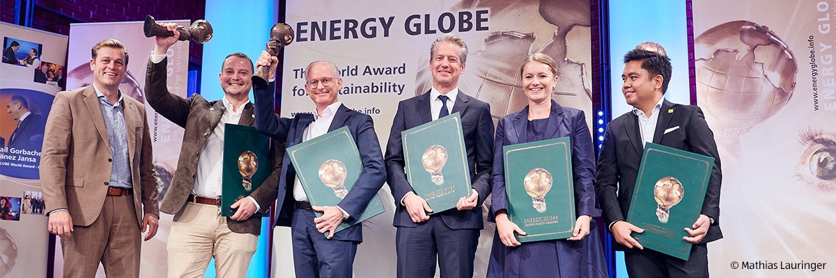 Sechs Personen auf Bühne mit Energy Globe-Auszeichnung, halten Urkunden, eine hebt eine Trophäe hoch.