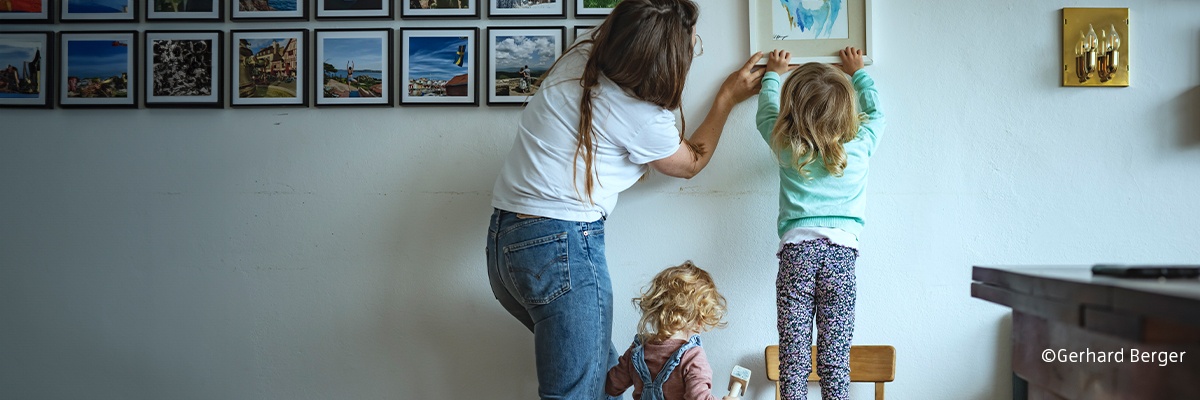 Eine Mutter hängt mit zwei Kindern ein Bild auf.