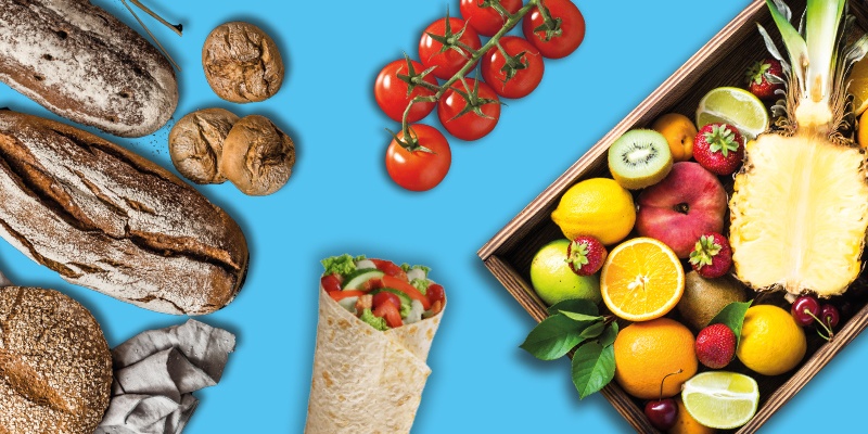 Verschiedene Lebensmittel auf blauem Hintergrund, darunter Brot, Gemüse, Obst und Nüsse.