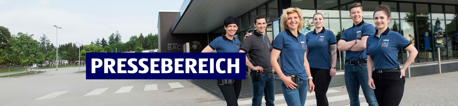 Eine Mitarbeiterin und ein Mitarbeiter mit verschränkten Armen vor einer HOFER Filiale
