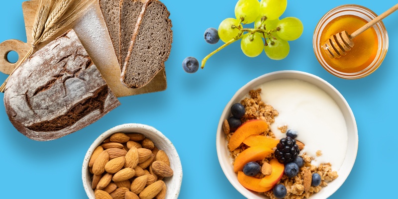 Brot, Joghurt mit Früchten, Honig, Nüsse und Trauben auf blauem Hintergrund