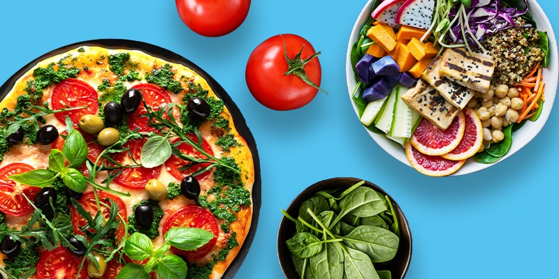 Vegane Pizza mit Tomaten und Basilikum und eine Schüssel mit aufgeschnittenen Obst.