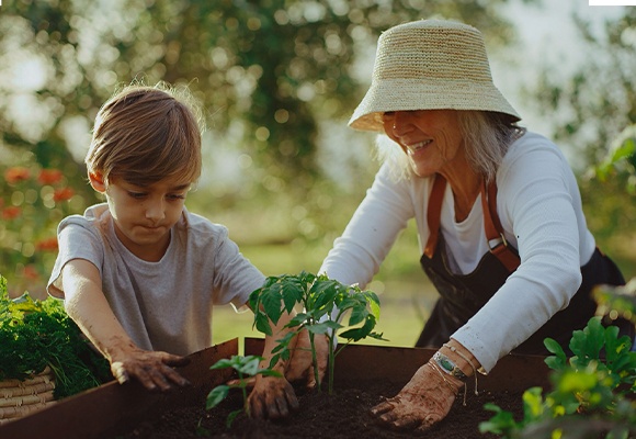 Zwei Personen gärtnern zusammen, eine mit Strohhut und Schürze, die andere mit kurzärmligem Shirt.