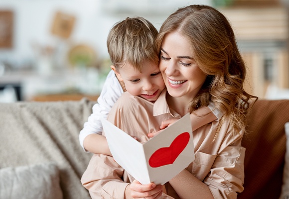 Zwei Personen sitzen auf dem Sofa, eine hält eine Karte mit rotem Herz, die andere schaut darauf.