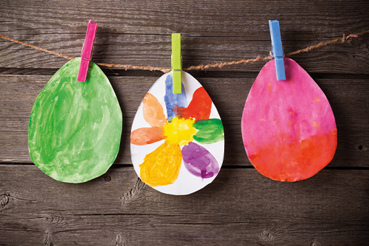 Es sind drei bemalte Ostereier aus Papier mit Wäscheklammern auf einer Schnur aufgehängt.