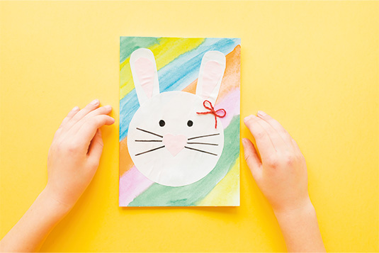 Gelber Hintergrund. Darauf liegt eine selbst gebastelte bunte Karte mit einem Osterhasen darauf