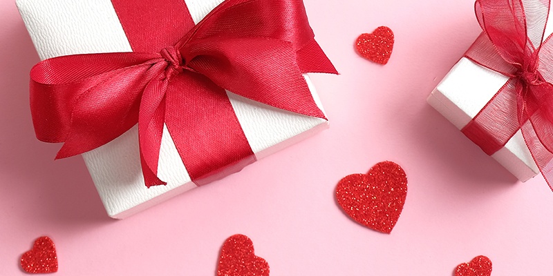 Weiße Geschenke mit roten Schleifen auf rosa Untergrund mit glitzernden Herzen