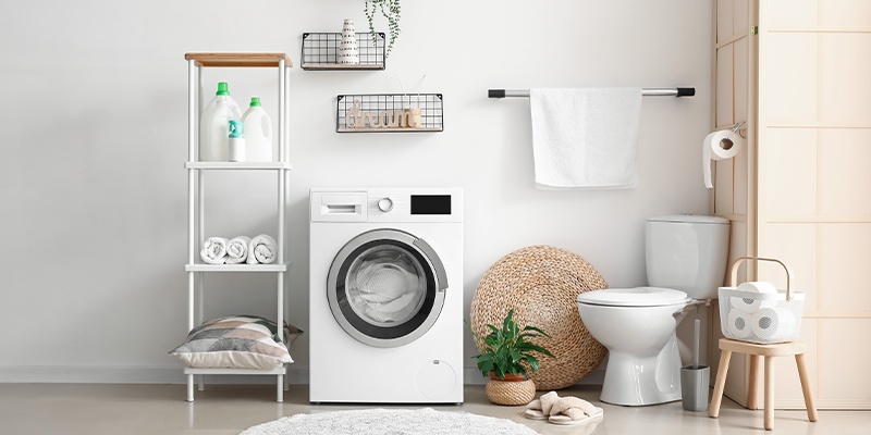 Aufgeräumtes Badezimmer mit Waschmaschine, Regal, Toilettenpapierhalter, Pflanze und Korb.