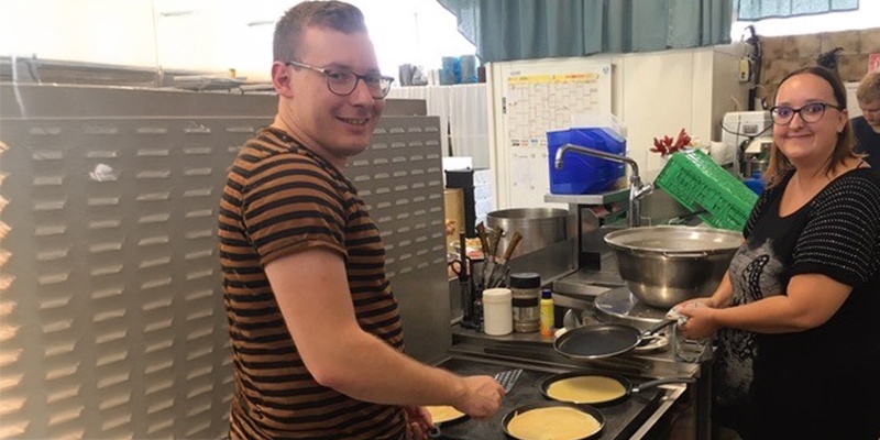 Man sieht zwei Personen, die in einer Küche kochen. 