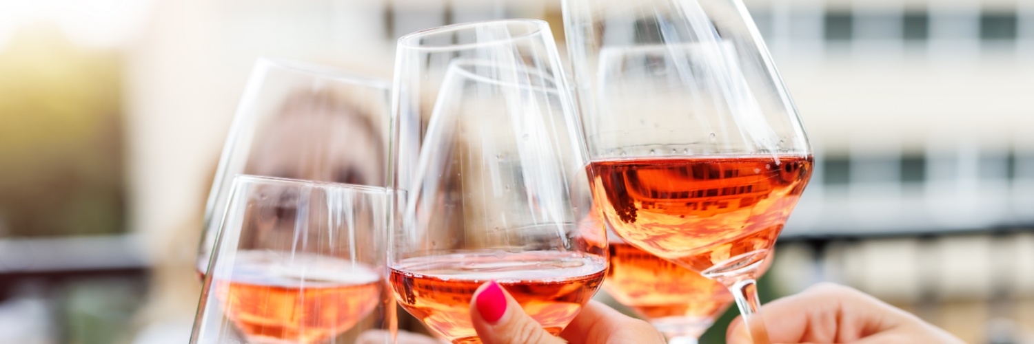 Drei Gläser Rosewein auf einem Holztisch, rote Weintrauben, Weingarten im Hintergrund